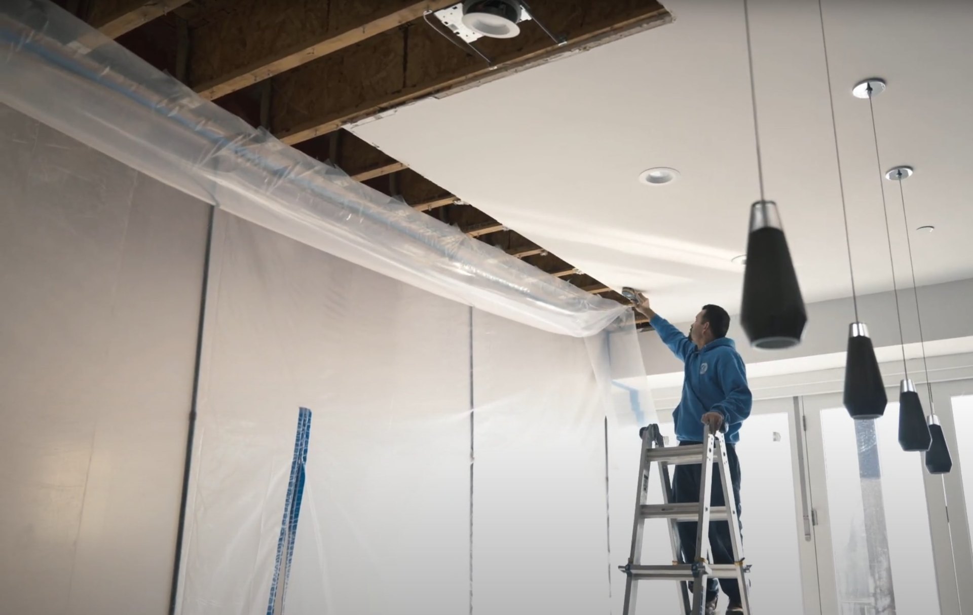 Water damage restoration technician working on exposed ceiling and HVAC systems with protective plastic sheeting