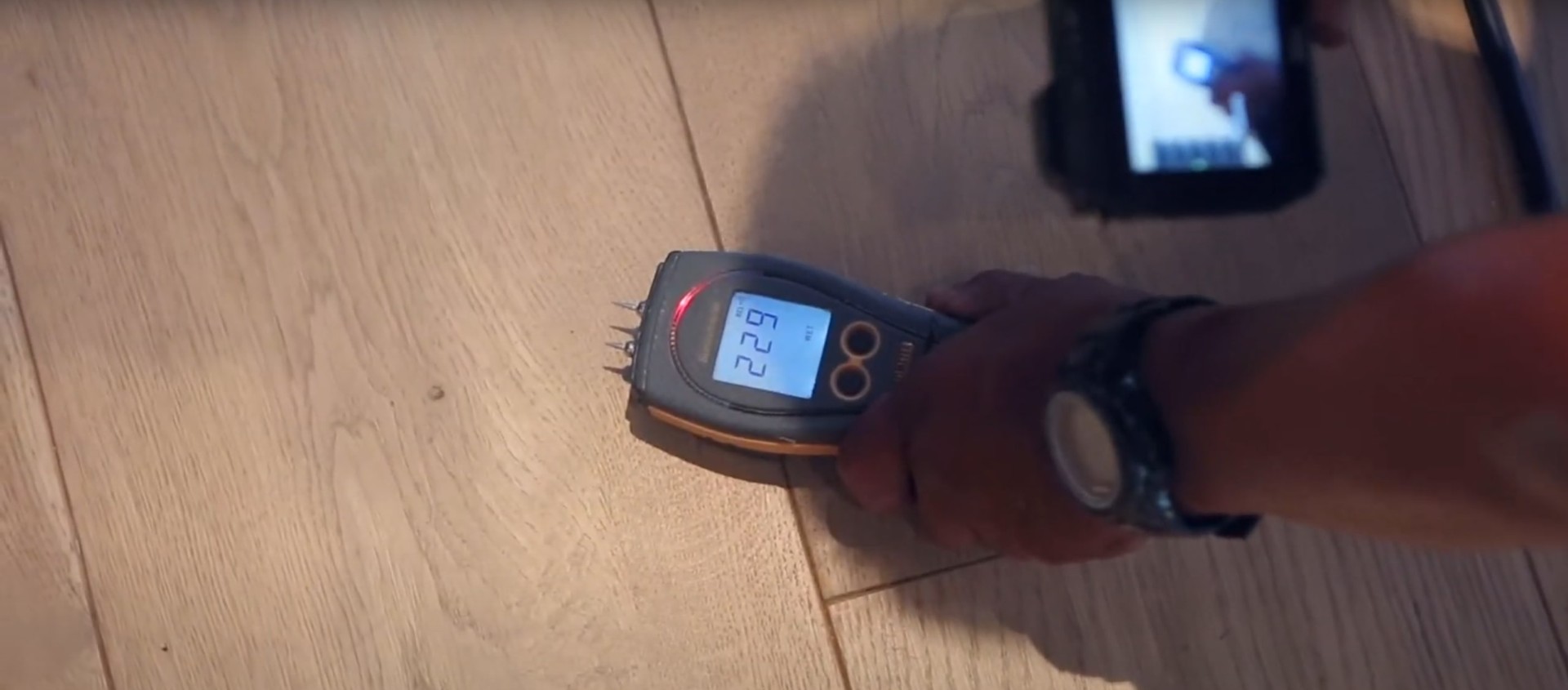 Professional moisture detection equipment showing readings on wooden floor surface during water damage assessment
