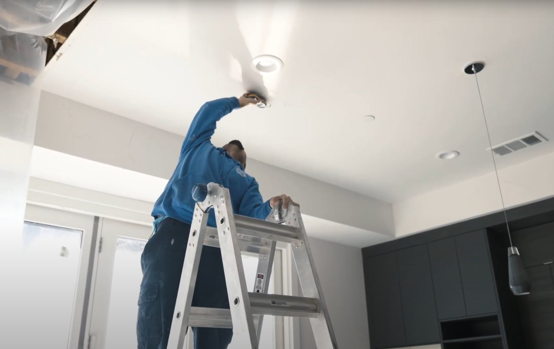 Professional water damage restoration technician working on ceiling repair with ladder and equipment